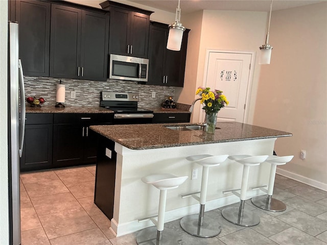 kitchen with backsplash, decorative light fixtures, appliances with stainless steel finishes, a kitchen bar, and a center island with sink