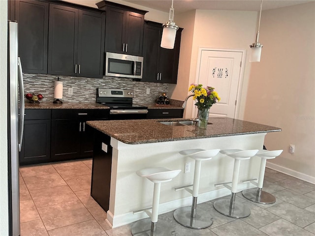 kitchen featuring tasteful backsplash, appliances with stainless steel finishes, a kitchen island with sink, a sink, and dark stone countertops