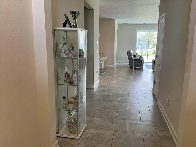 hallway with tile patterned flooring, baseboards, and a textured ceiling