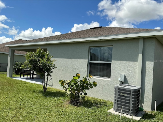 view of property exterior featuring roof with shingles, a patio, stucco siding, a lawn, and central AC unit