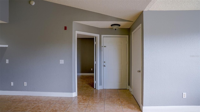 spare room with vaulted ceiling, light tile patterned floors, baseboards, and a textured ceiling