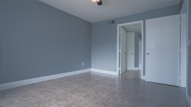 empty room featuring a ceiling fan, visible vents, baseboards, tile patterned flooring, and a textured ceiling