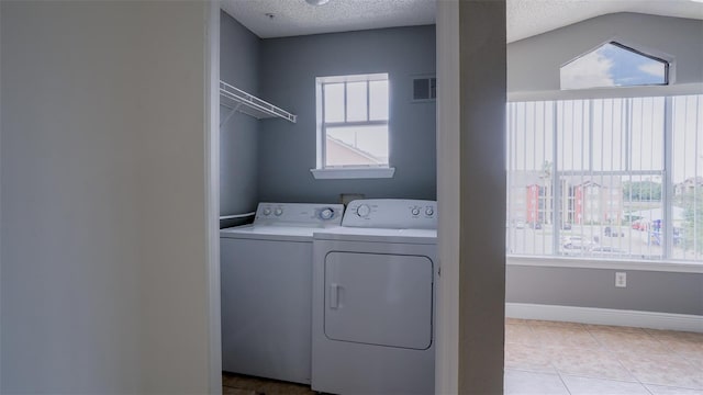 clothes washing area featuring visible vents, baseboards, washing machine and dryer, light tile patterned floors, and a textured ceiling