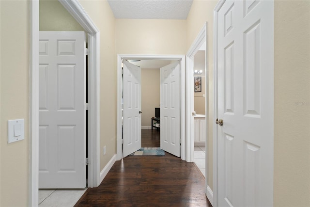 corridor featuring a textured ceiling, baseboards, and wood finished floors