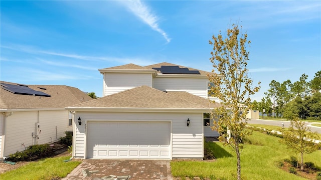 traditional home with a garage, solar panels, a shingled roof, decorative driveway, and a front lawn