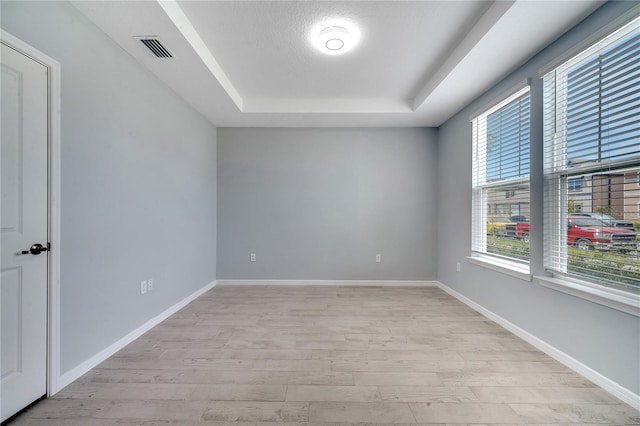 empty room with a tray ceiling, visible vents, light wood-style flooring, and baseboards