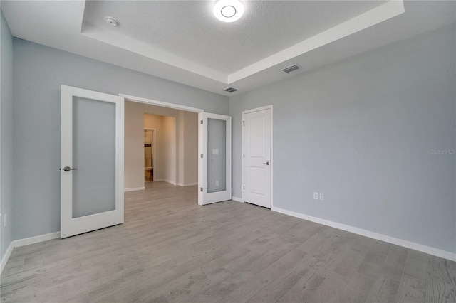 unfurnished bedroom with baseboards, visible vents, a raised ceiling, and wood finished floors