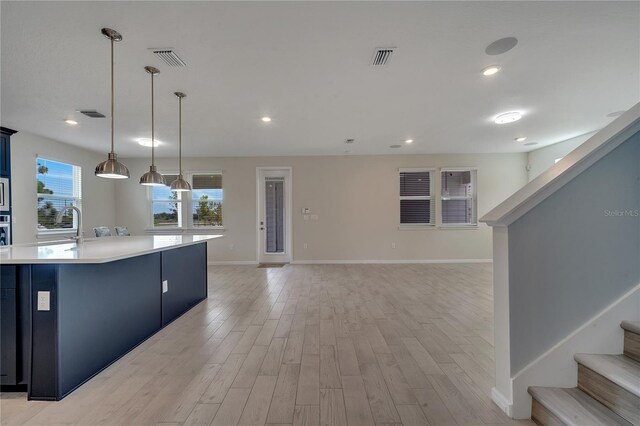 kitchen with a kitchen island, sink, decorative light fixtures, and light hardwood / wood-style floors