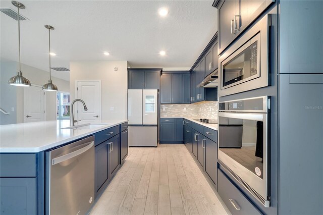 kitchen with light wood-type flooring, tasteful backsplash, stainless steel appliances, an island with sink, and sink