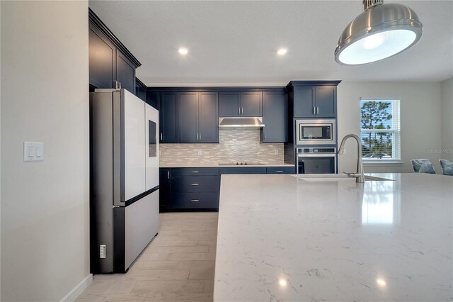 kitchen with light stone counters, stainless steel appliances, tasteful backsplash, a sink, and under cabinet range hood