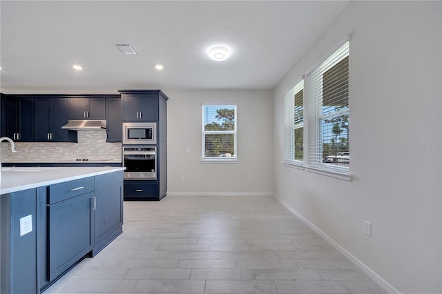 kitchen with visible vents, appliances with stainless steel finishes, light countertops, under cabinet range hood, and backsplash