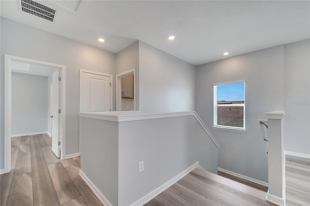 hallway with baseboards, visible vents, light wood-style flooring, and an upstairs landing