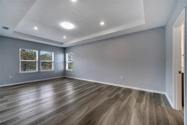 unfurnished room featuring a raised ceiling, visible vents, dark wood finished floors, and baseboards