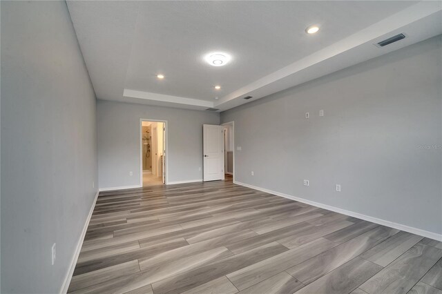 empty room with a raised ceiling and light hardwood / wood-style floors