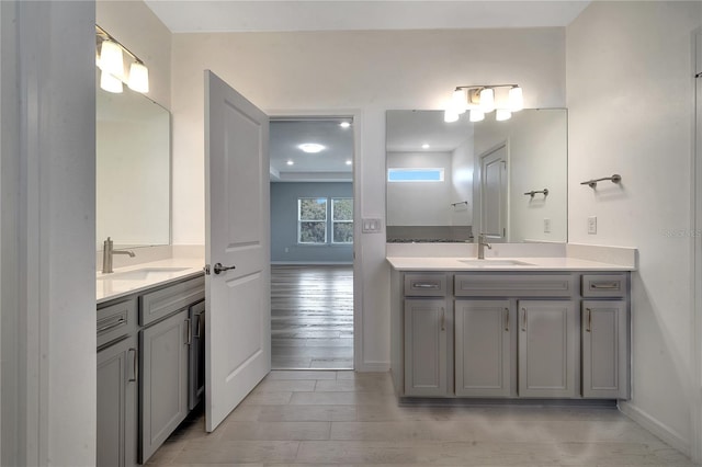 full bath with two vanities, a sink, baseboards, and wood finished floors