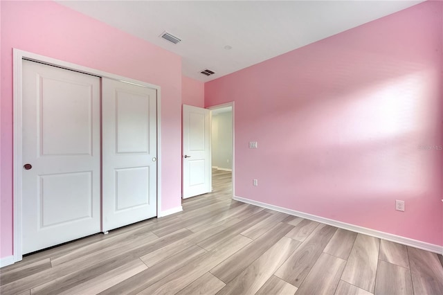 unfurnished bedroom featuring light wood-type flooring, a closet, visible vents, and baseboards