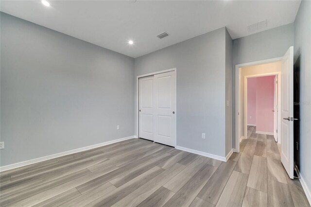 unfurnished bedroom featuring a closet, baseboards, visible vents, and light wood finished floors