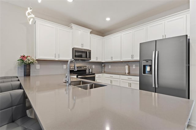 kitchen featuring decorative light fixtures, appliances with stainless steel finishes, white cabinetry, kitchen peninsula, and a kitchen bar