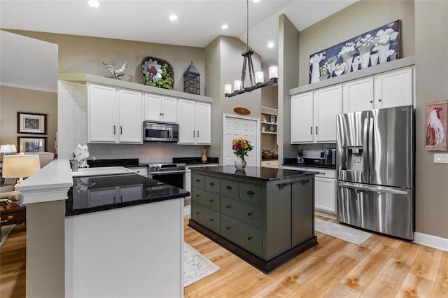 kitchen featuring appliances with stainless steel finishes, a peninsula, a high ceiling, white cabinetry, and a sink