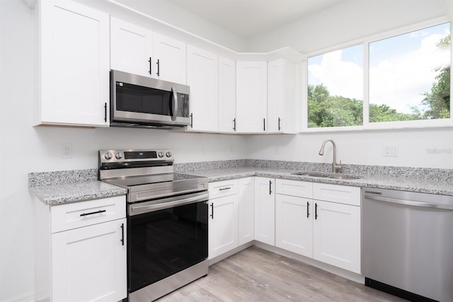 kitchen with stainless steel appliances, sink, white cabinetry, and light hardwood / wood-style flooring