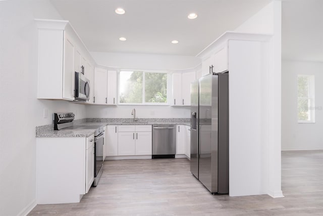 kitchen with white cabinets, light hardwood / wood-style flooring, appliances with stainless steel finishes, light stone countertops, and sink