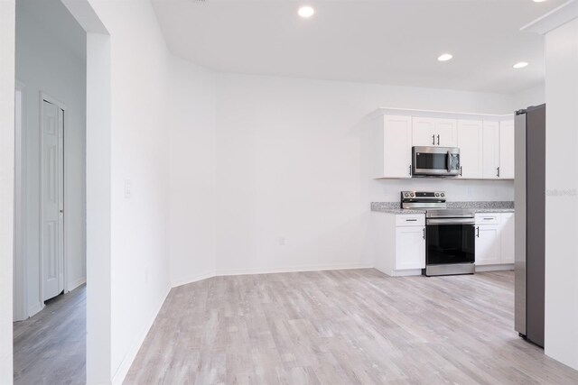 kitchen with white cabinetry, stainless steel appliances, light stone countertops, and light hardwood / wood-style floors