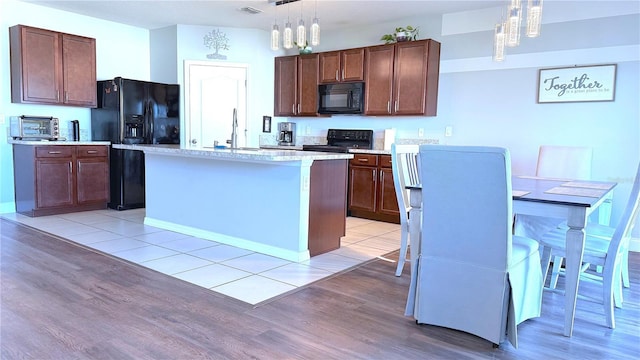 kitchen with black appliances, pendant lighting, light hardwood / wood-style floors, and an island with sink