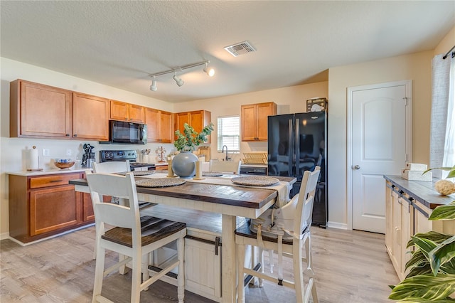 kitchen featuring black appliances, a textured ceiling, light hardwood / wood-style flooring, and track lighting