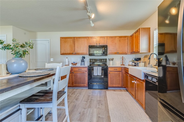 kitchen featuring a textured ceiling, rail lighting, black appliances, sink, and light hardwood / wood-style floors