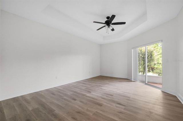 unfurnished room featuring a raised ceiling, ceiling fan, and hardwood / wood-style flooring