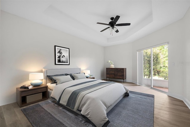 bedroom with hardwood / wood-style floors, ceiling fan, a tray ceiling, and access to outside