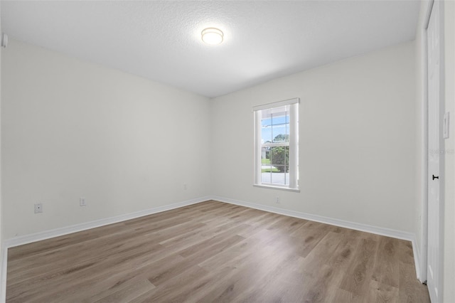 empty room with a textured ceiling and light hardwood / wood-style flooring