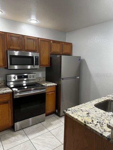 kitchen featuring a textured ceiling, light tile patterned floors, light stone countertops, and appliances with stainless steel finishes