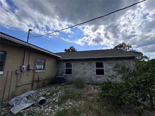 view of property exterior featuring a shingled roof, cooling unit, and concrete block siding