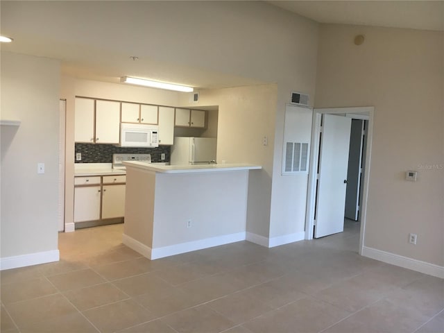 kitchen with white appliances, tasteful backsplash, light tile patterned floors, kitchen peninsula, and a towering ceiling