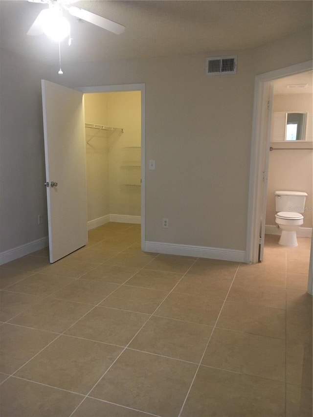 unfurnished bedroom featuring a walk in closet, ceiling fan, light tile patterned floors, and a closet