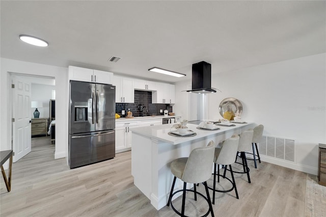 kitchen featuring stainless steel refrigerator with ice dispenser, island range hood, a kitchen bar, and white cabinets