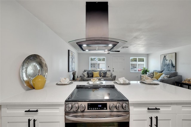 kitchen with light stone counters, island exhaust hood, white cabinetry, and stainless steel stove