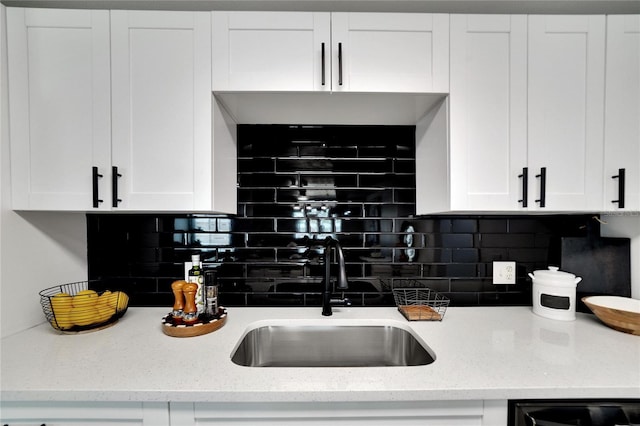 kitchen featuring tasteful backsplash, light stone counters, sink, and white cabinets