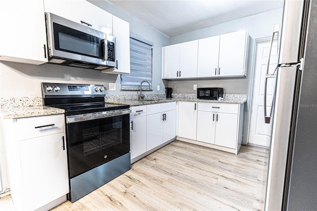 kitchen with light wood-type flooring, light stone countertops, stainless steel appliances, and white cabinetry