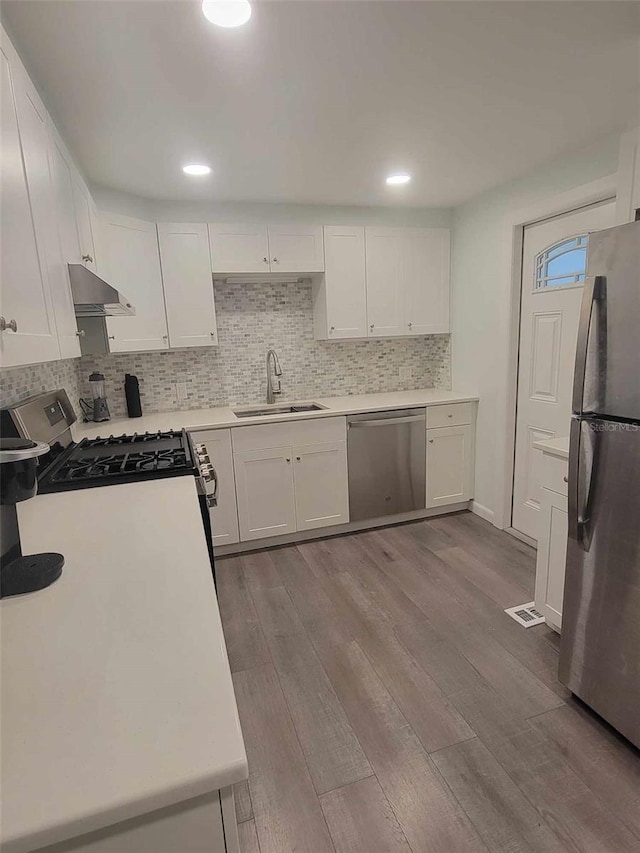 kitchen with backsplash, light hardwood / wood-style floors, stainless steel appliances, sink, and white cabinetry