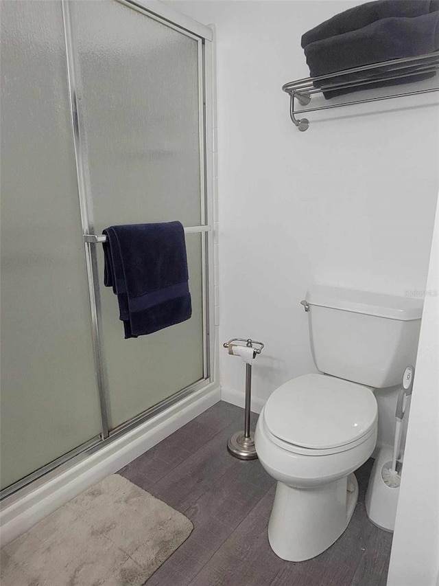 bathroom featuring a shower with shower door, toilet, and wood-type flooring