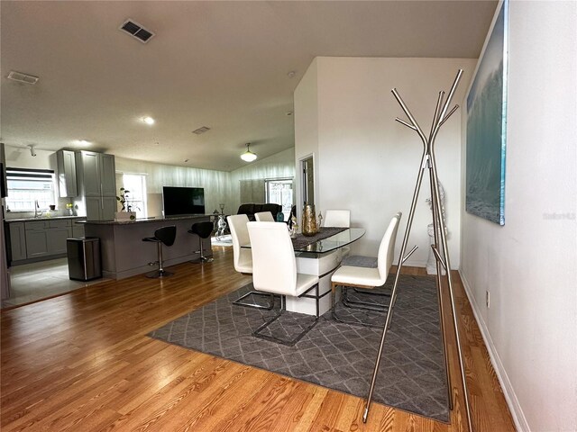 dining area featuring sink, hardwood / wood-style flooring, and vaulted ceiling