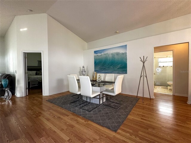 dining space with dark wood-type flooring, vaulted ceiling, and a textured ceiling