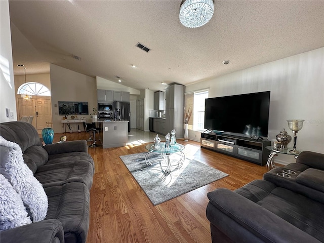 living room with lofted ceiling, a textured ceiling, and light hardwood / wood-style floors