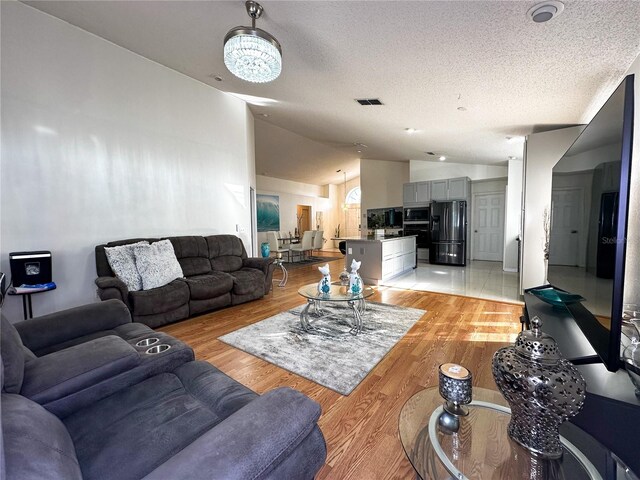 living room featuring light hardwood / wood-style flooring, a textured ceiling, and vaulted ceiling