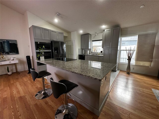 kitchen featuring dark stone counters, sink, black appliances, vaulted ceiling, and gray cabinets