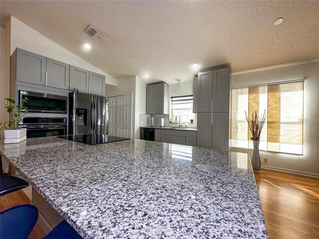 kitchen with light stone counters, lofted ceiling, black appliances, and a kitchen breakfast bar