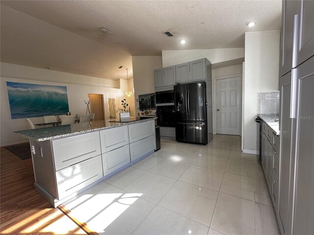 kitchen featuring lofted ceiling, refrigerator with ice dispenser, gray cabinets, light stone counters, and a textured ceiling