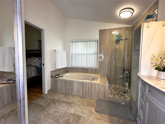 bathroom featuring independent shower and bath, vanity, vaulted ceiling, and a textured ceiling